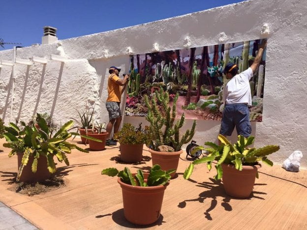 Dos hombres ponen una lona de la exposición de Rodalquilarte en la fachada de una casa del municipio.