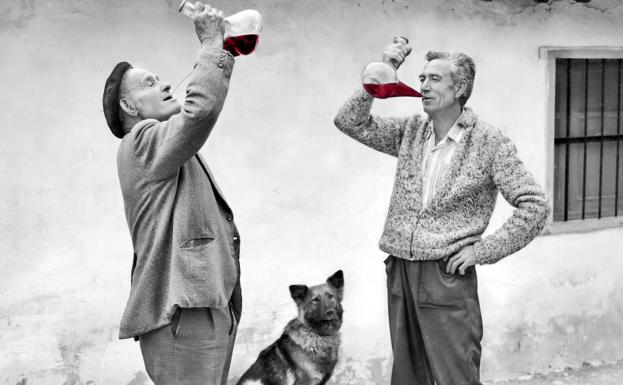 Dos hombres beben vino con sus porrones. 